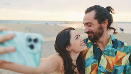 Laughing couple taking selfie on mobile phone while standing on the beach