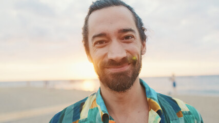Close-up of young smiling man looking at the camera on the beach at sunrise