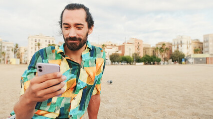 Young man sitting and using mobile phone on the beach