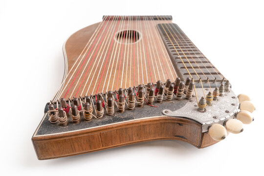 High angle closeup horizontal studio shot of vintage, old wooden zither isolated on white background. Detail of zither mechanics and tuning pins. Dusty and scratched instrument.