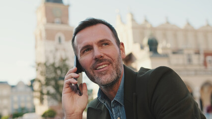 Close up, happy middle aged man talking on mobile phone on old town background