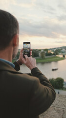 Man takes video of the picturesque river bank. Back view