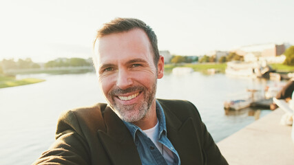 Close up, man makes selfie on mobile phone on the embankment of the river. Backlight
