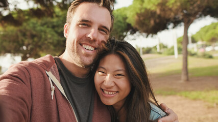 Close up, laughing couple hugging each other while standing in the park. looking at camera