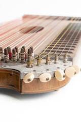 High angle vertical studio shot of vintage, old wooden zither isolated on white background. Detail of zither mechanics and tuning pins. Dusty and scratched musical instrument.