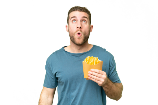 Young handsome blonde man holding fried chips over isolated chroma key background looking up and with surprised expression