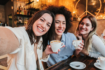 Group of three happy young women taking a selfie portrait on a coffee shop. Multi ethnic friends...