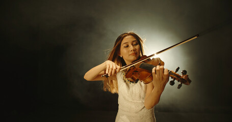 Female violin player performing sheet music on stage. Experienced asian violin player having solo concert, spotted by light on black background 