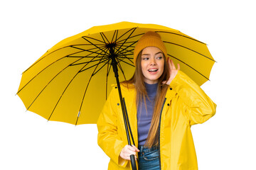 Young pretty woman with rainproof coat and umbrella over isolated chroma key background listening to something by putting hand on the ear