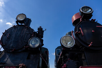 Front view of two steam locomotives standing side by side. Bottom view showing objects against a blue sky