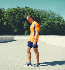 Sport and healthy lifestyle concept - sporty fitness runner man standing in the city park, ready for working or resting after run training outdoors