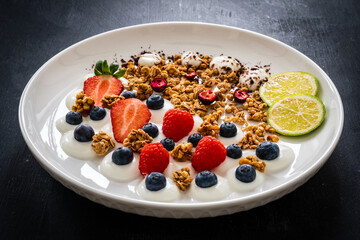 Yogurt with strawberries, blueberries, raspberries and muesli in bowl on wooden table
