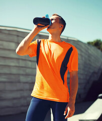 Portrait of tired young runner man drinking from bottle the water or protein shake, male sportsman...