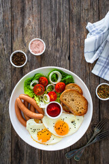 Breakfast - sunny side up egg, boiled sausages and vegetables served on wooden table
