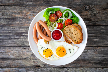 Breakfast - sunny side up egg, boiled sausages and vegetables served on wooden table
