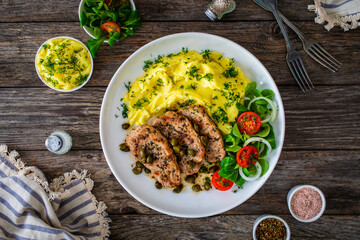 Fried pork loin with mashed potatoes and vegetables on wooden table
