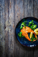 Fried salmon steak and fresh vegetable salad served on wooden table
