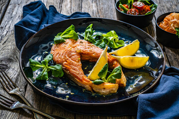 Fried salmon steak and fresh vegetable salad served on wooden table
