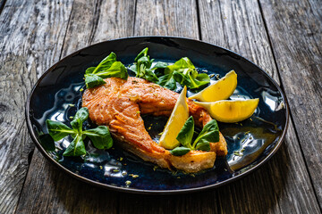 Fried salmon steak and fresh vegetable salad served on wooden table
