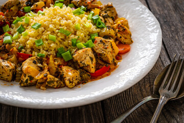 Fried chicken nuggets, bulgur groats, carrots and red pepper on wooden background
