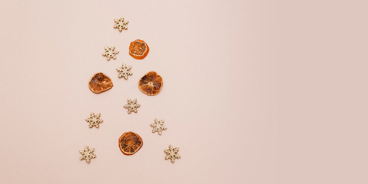 Candied citrus fruits and golden snowflakes are laid out in the shape of a Christmas tree on a beige background. Minimalistic greeting card for New Year and Christmas. Copy space. Flatley. Top view