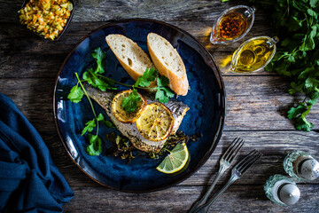 Roast sea bream with bread and lemon on wooden table
