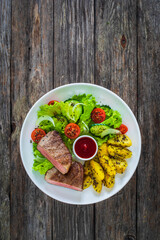Fried beef sirloin with  potatoes and vegetables on wooden table
