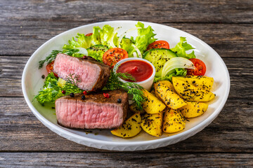 Fried beef sirloin with  potatoes and vegetables on wooden table

