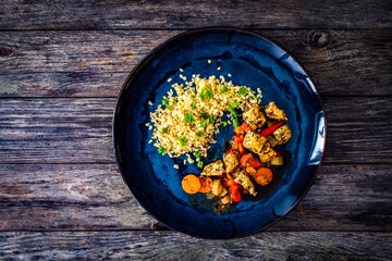 Fried chicken nuggets, bulgur groats, carrots and red pepper on wooden background
