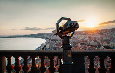 Coin-operated binoculars by balusters against cityscape and sky during sunset