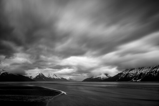 Clouds and water moving past snow covered mountains.   Alaska, USA.