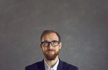 Portrait of unsure male employee with funny dreamy facial expression on gray background. Close up...