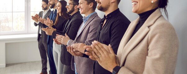 Happy audience applauding speaker at business conference or corporate team meeting. Group of people in formal suits standing in row in office, clapping hands and smiling. Banner, header background