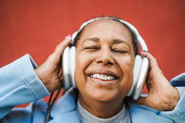 African senior woman listen playlist music with headphones outdoor - Main focus on eyes