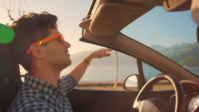 Careless relaxed man in sunglasses driving cabriolet car at fantastic golden sunset. Sun flare. Concept of success, tourism, rental cars. Happy smiling tourist travel in California. Summer vacation