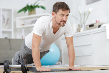 cheerful muscular man in living room practicing in plank position