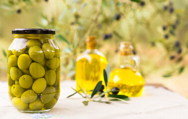 canned olives in a glass jar, oil and olives on the table against the background of the olive garden
