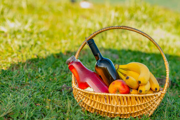 picnic basket with wine, juice and fruits on green grass