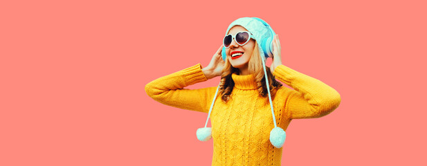 Winter portrait of cheerful young woman in wireless headphones listening to music wearing yellow...