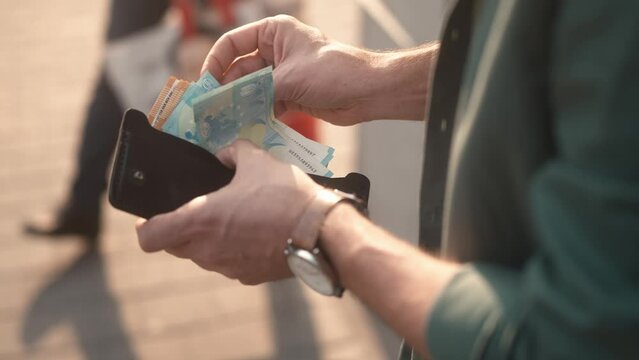 Close-up view of man looking at wallet counting euro notes planning budget standing outside. Young adult caucasian male holding money cashed out from card. Currency concept.