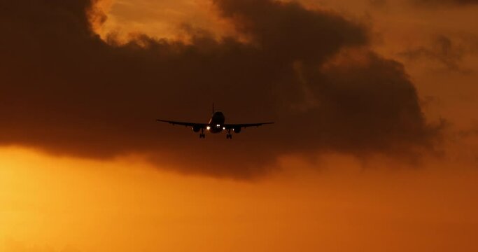 Black silhouette of an airplane in a bright orange sunset sky. Aerobatics of professional pilots on board a large passenger aircraft. The silhouette of a passenger plane flown by experienced pilots.