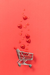 Valentine's day concept. Shopping trolley with gift boxes, roses, chocolate and red hearts on red...