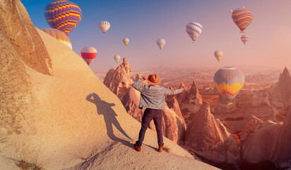 Young hiker man in hat on top mountain background hot air balloons in Cappadocia Turkey travel,...