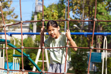 Asian girl playing climbing rope net in playground. Concept playground, child development, sports and recreation. Soft and selective focus. 