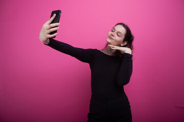 A young and cute woman without makeup takes a selfie on a mobile phone. The girl smiles sweetly.