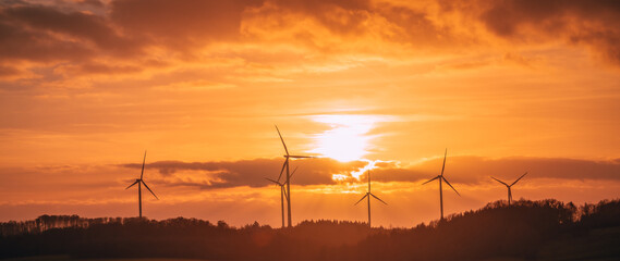 silhouette of wind turbines under the orange sky at sunset