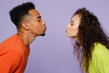 Side view young couple two friends family man woman of African American ethnicity wear casual clothes together kiss each other with closed eyes stand face to face isolated on plain purple background.