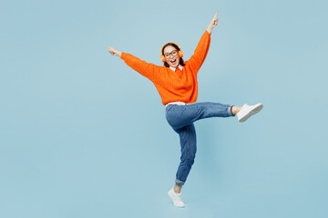 Full body side view young woman of Asian ethnicity wear orange sweater glasses listen to music in...