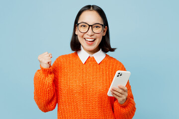 Young overjoyed happy woman of Asian ethnicity in orange sweater glasses hold in hand use mobile...