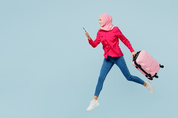 Traveler arabian asian muslim woman wear pink abaya hijab hold mobile cell phone bag isolated on plain blue background Tourist travel abroad in free time rest getaway Air flight trip journey concept.